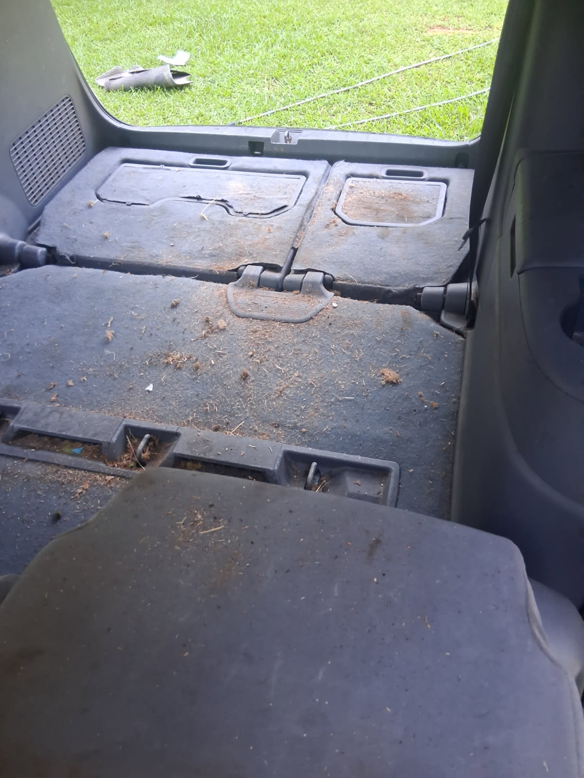 Dirty minivan cargo area before detailing — dusty carpet, debris and folded third-row seats